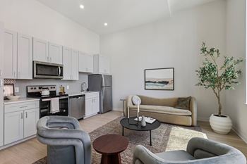 A modern living room with grey and white furniture and a kitchen area in the background.